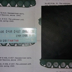 Puede incluir: Una hoja de kit de modelo con ilustraciones de tanques y texto en ruso e inglés. Una hoja negra con patrones circulares está a la derecha. Una hoja de calcomanías azul claro con números y letras está en el centro.