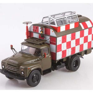 May include: A green military truck with a white and red checkered box on the back. The box has a clear plastic roof and a red and white striped design. The truck has a black grill and black wheels.