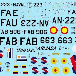 Op de afbeelding: Een vel modelvliegtuigdecals met verschillende markeringen, waaronder de woorden "NAVAL", "FAE", "FAU", "FAB-906", "FAB 663", "ARMADA", "AN-223" en "272". De decals zijn in zwart, rood, geel, blauw, groen en wit.