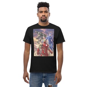 May include: Black t-shirt featuring a colorful graphic of three armored figures against a cloudy sky. The central figure is red and gold, flanked by a silver and a blue armored character. The t-shirt is made of a thick, comfortable material.