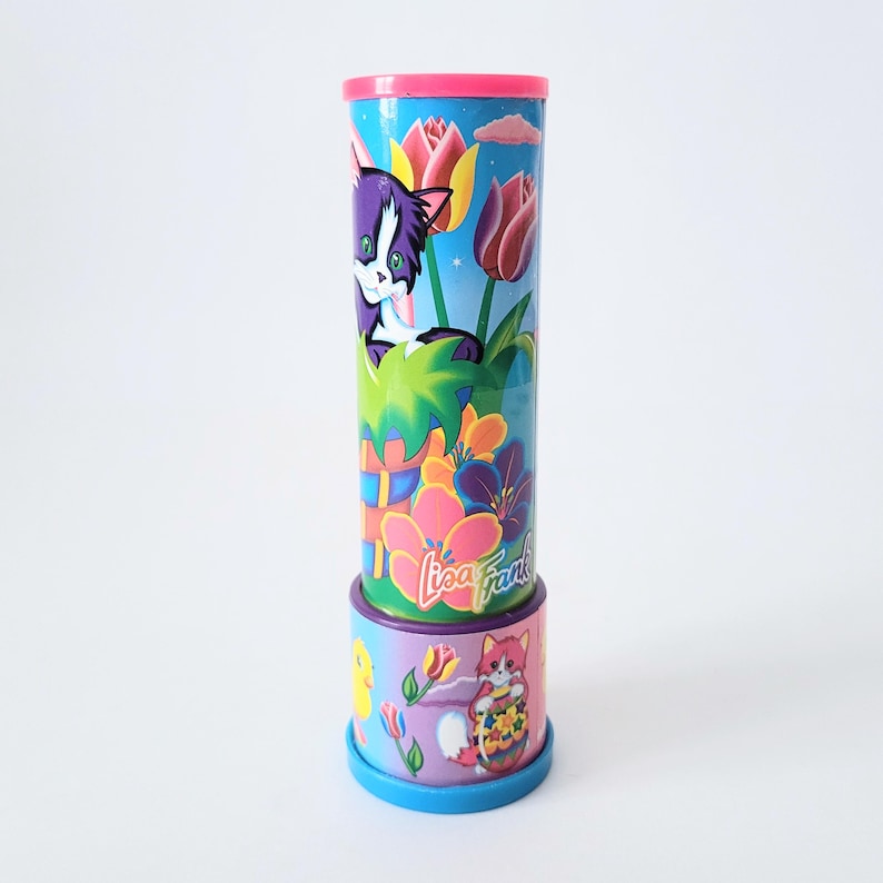 Op de afbeelding: Een cilindrische Lisa Frank-kaleidoscoop met een roze bovenkant en een blauwe basis. De behuizing heeft een cartoonkat, bloemen en het Lisa Frank-logo. De basis heeft een cartoonvos en een eend.