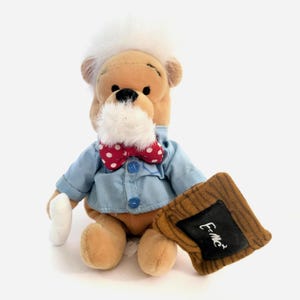 May include: A plush bear toy dressed as a professor, wearing a light blue shirt, red polka dot bow tie, and a white wig and beard. The bear holds a small chalkboard with "E=mc²" written on it.