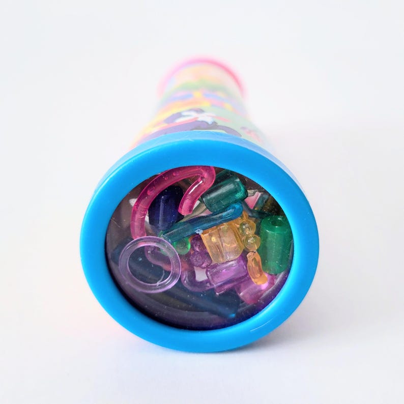 Op de afbeelding: Een kleurrijke caleidoscoop met een blauw oculair en een roze rand. De buis is versierd met een patroon van verschillende kleuren. De caleidoscoop is gevuld met kleine, kleurrijke, doorschijnende vormen in tinten roze, groen, blauw en oranje.