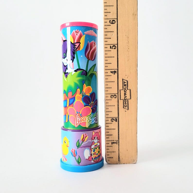 Op de afbeelding: Een Lisa Frank-kaleidoscoop met een roze en blauw ontwerp. De kaleidoscoop heeft een paarse kat, bloemen en het Lisa Frank-logo. De kaleidoscoop is ongeveer 15 cm hoog.