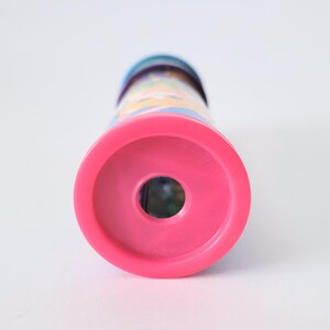 Op de afbeelding: Een roze caleidoscoop met een kleurrijk patroon. De caleidoscoop heeft een cirkelvormig roze uiteinde en een cilindrisch lichaam met een levendig, veelkleurig patroon. Het speelgoed is ontworpen voor het bekijken van kleurrijke patronen.