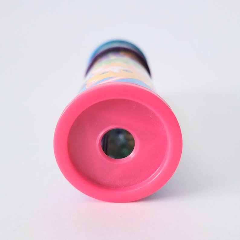 Op de afbeelding: Een roze caleidoscoop met een kleurrijk patroon. De caleidoscoop heeft een cirkelvormig roze uiteinde en een cilindrisch lichaam met een levendig, veelkleurig patroon. Het speelgoed is ontworpen voor het bekijken van kleurrijke patronen.