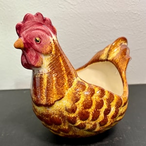 May include: A ceramic chicken planter with brown and yellow speckled paint and a red comb. The planter has a white interior and is shaped like a hen.