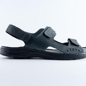 May include: A single dark gray sandal with adjustable straps. The sandal features a textured sole and multiple cut-out details. The straps are secured with hook-and-loop closures. The sandal is designed for comfort and support.