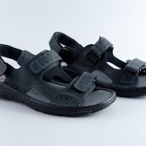 May include: A pair of black leather sandals with adjustable straps. The sandals have a textured sole and are designed for comfort and support. The straps feature a hook-and-loop closure for a secure fit. Ideal for casual wear.