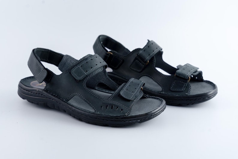 May include: A pair of black leather sandals with adjustable straps. The sandals have a textured sole and are designed for comfort and support. The straps feature a hook-and-loop closure for a secure fit. Ideal for casual wear.