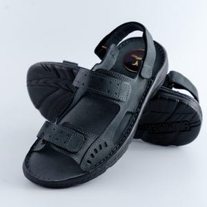 May include: A pair of black leather sandals with adjustable straps and a textured sole. The sandals have a hook-and-loop closure and a small logo on the insole. The sandals are designed for comfort and support.