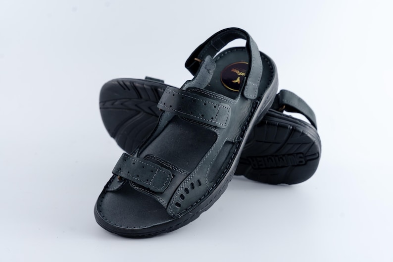 May include: A pair of black leather sandals with adjustable straps and a textured sole. The sandals have a hook-and-loop closure and a small logo on the insole. The sandals are designed for comfort and support.