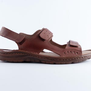 May include: Brown leather sandal with adjustable straps. The sandal features a contoured footbed and a durable sole. The design includes multiple straps and a hook-and-loop closure for a secure fit. Ideal for casual wear.