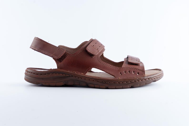 May include: Brown leather sandal with adjustable straps. The sandal features a contoured footbed and a durable sole. The design includes multiple straps and a hook-and-loop closure for a secure fit. Ideal for casual wear.