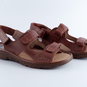 May include: A pair of brown leather sandals with adjustable straps. The sandals have a hook-and-loop closure and a textured sole. The open-toe design is ideal for warm weather.