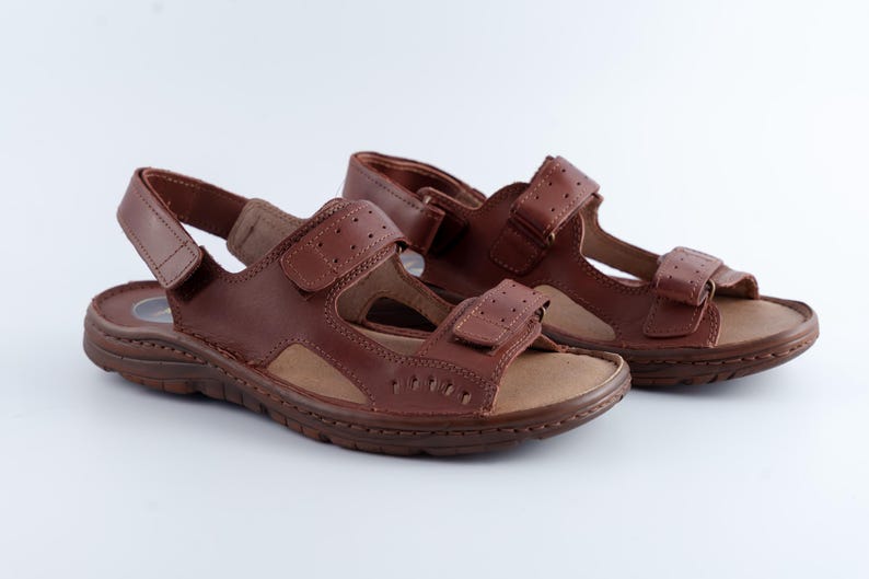 May include: A pair of brown leather sandals with adjustable straps. The sandals have a hook-and-loop closure and a textured sole. The open-toe design is ideal for warm weather.
