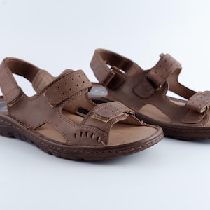 May include: A pair of brown leather sandals with adjustable straps and hook-and-loop closures. The sandals have a textured footbed and a durable sole, suitable for outdoor wear.