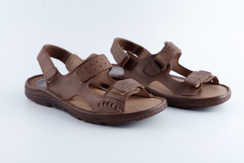 May include: A pair of brown leather sandals with adjustable straps and hook-and-loop closures. The sandals have a textured footbed and a durable sole, suitable for outdoor wear.