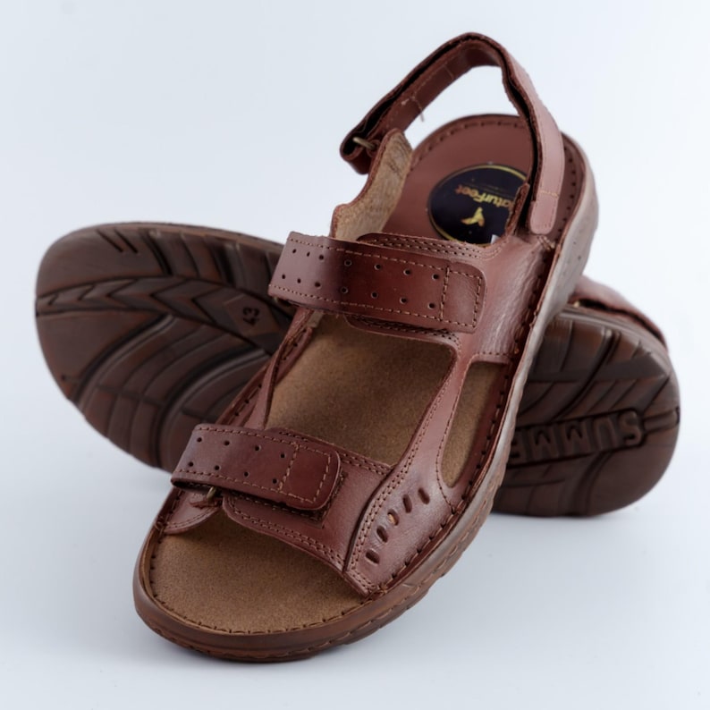 May include: Brown leather sandals with adjustable straps and a textured sole. The sandals feature a hook-and-loop closure for a secure fit. The sole is marked with the word "SUMMIT".