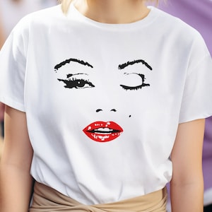 May include: White t-shirt with a black and white graphic of a woman's face with red lips. The woman is winking with one eye.