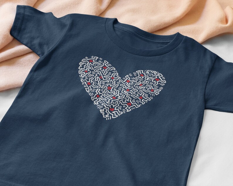 Pode incluir: Uma camiseta azul marinho com um design branco em forma de cora&ccedil;&atilde;o. O cora&ccedil;&atilde;o &eacute; feito de pequenas figuras repetidas.