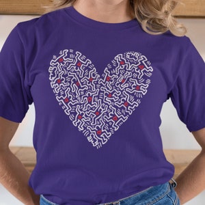 Pode incluir: Camiseta roxa com um design em forma de cora&ccedil;&atilde;o branco que apresenta um padr&atilde;o de figuras estilizadas. O design do cora&ccedil;&atilde;o tem pequenos cora&ccedil;&otilde;es vermelhos espalhados por todo.