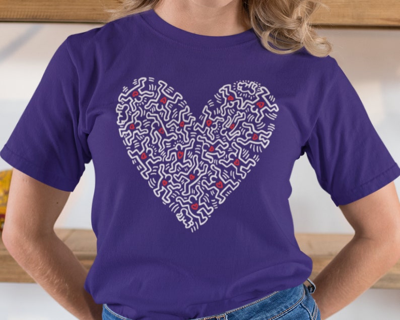 Pode incluir: Camiseta roxa com um design em forma de cora&ccedil;&atilde;o branco que apresenta um padr&atilde;o de figuras estilizadas. O design do cora&ccedil;&atilde;o tem pequenos cora&ccedil;&otilde;es vermelhos espalhados por todo.