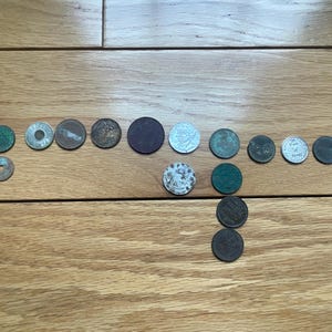 May include: A collection of antique coins of various sizes and colors, including copper, silver, and bronze. The coins are arranged on a wooden surface, showcasing their different designs and levels of wear. Some coins have visible markings and details.