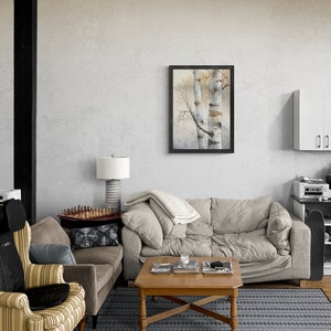May include: A living room with a grey sofa, a brown armchair, a coffee table, and a framed watercolour painting of two birch trees. The room has a wooden floor and a grey rug with a black pattern.