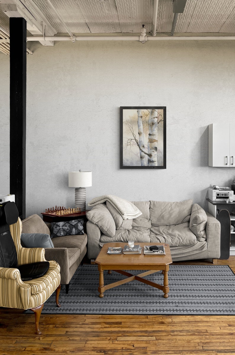 May include: A living room with a grey sofa, a brown armchair, a coffee table, and a framed watercolour painting of two birch trees. The room has a wooden floor and a grey rug with a black pattern.