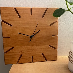Könnte beinhalten: Eine Wanduhr aus Holz mit schwarzen Zeigern und einem einzigartigen Design mit Ausschnitten um das Zifferblatt.