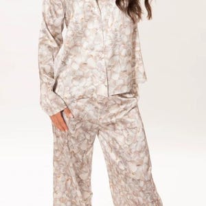May include: A white satin pyjama set with a shell print. The top has long sleeves and a button-up front. The trousers are wide-legged and have a relaxed fit.