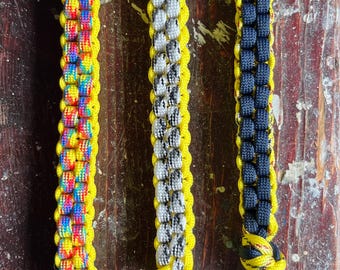 Puede incluir: Tres llaveros hechos con paracord de colores. Los llaveros son amarillos, blancos y negros, y azules y amarillos. Cada llavero tiene un anillo de metal plateado y un cierre de metal plateado.