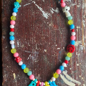 May include: A colorful beaded necklace with a variety of charms, including a dice, a mushroom, a smiley face, and the word "PISSY" spelled out in colorful letters.