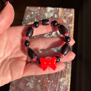 Puede incluir: Un brazalete de cuentas negras con detalles rojos y un dije de lazo rojo.