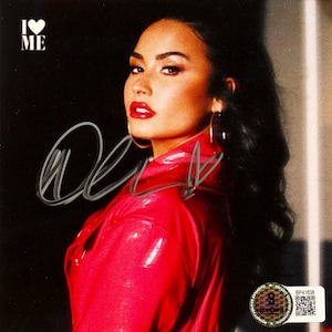 May include: A signed photograph of a woman wearing a red leather jacket. The woman is looking to the left of the camera. The text "I ♥ ME" is in the top left corner of the image. The image is signed "Demi".