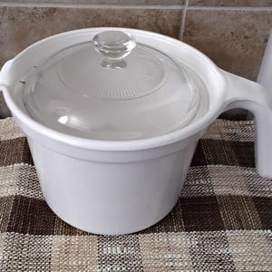 May include: A white ceramic mug with a black handle and the text "But First, Coffee" in a handwritten style. The mug is on a white surface. The mug is 4 inches tall.