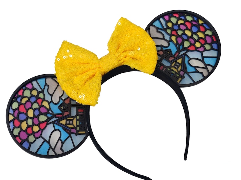 May include: Black headband with a yellow bow and two black ears. Each ear has a stained glass design of a house with balloons.