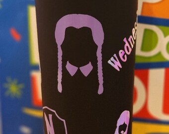 Puede incluir: Un termo de viaje negro con una silueta morada de Wednesday Addams de la familia Addams. El termo tiene un fondo blanco y el texto "Wednesday" está escrito en el lateral.