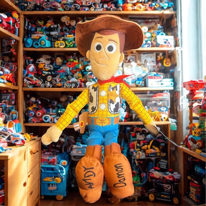 Puede incluir: Mu&ntilde;eco de peluche de Woody de la franquicia Toy Story. El mu&ntilde;eco presenta un sombrero de vaquero marr&oacute;n, una camisa amarilla con un chaleco con estampado de vaca, pantalones azules y botas naranjas con los nombres "Andy" y "Damon" impresos. Un pa&ntilde;uelo rojo est&aacute; atado alrededor del cuello.