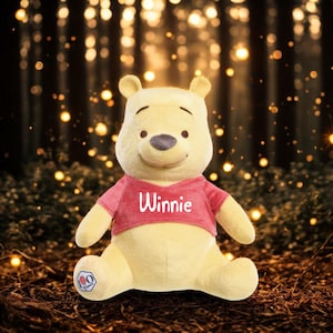Può includere: Un peluche di Winnie the Pooh, con corpo giallo e maglietta rossa con il nome "Winnie" stampato. Piccolo logo sul piede. Lo sfondo è una scena di foresta sfocata con luci bokeh.