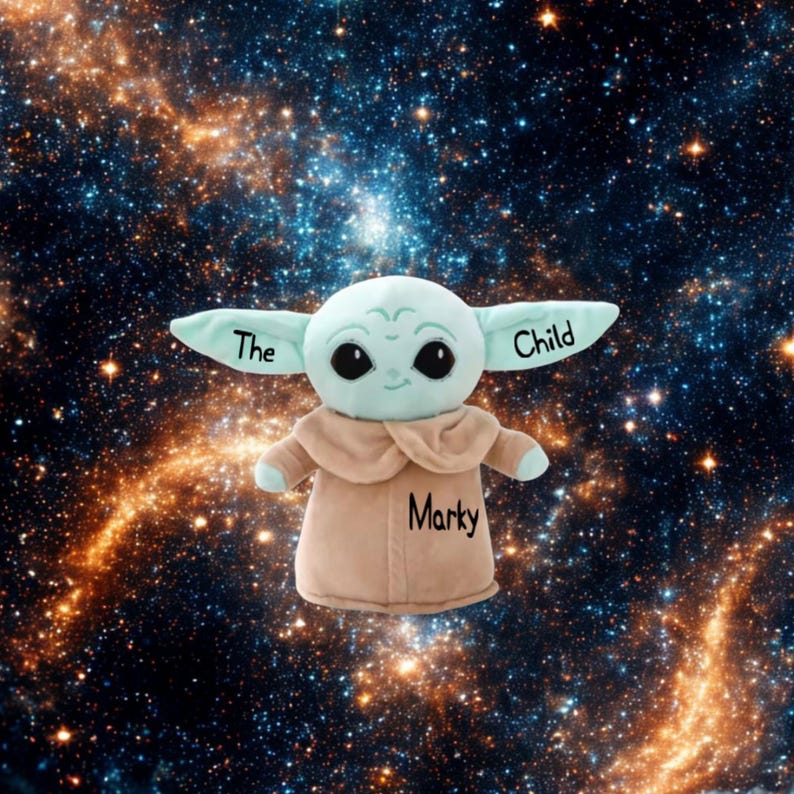 May include: A soft toy of a character with large ears, green skin, and large black eyes. The toy is wearing a tan robe and has the words "The Child" on its ears and the name "Marky" on its chest. The background is a galaxy of stars.