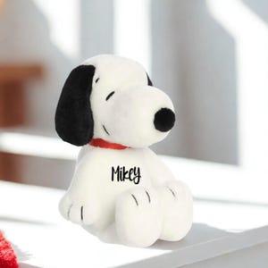 May include: A plush white dog with black ears and a black nose, wearing a red collar. The name "Mikey" is printed on the dog's chest. The dog is sitting down with its eyes closed.