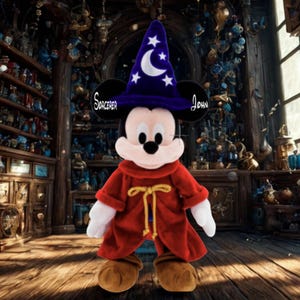 May include: A plush Mickey Mouse dressed as a sorcerer, wearing a blue hat with stars and a crescent moon. He has a red robe with a gold tie. The text "Sorcerer John" is on his ears.