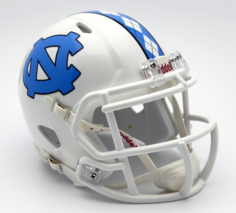 May include: A white football helmet with a blue logo and a blue and white argyle pattern on the top. The helmet has a white face mask and chin strap. The logo is a stylized letter "N" and "C" intertwined.