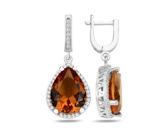 May include: A pair of silver-toned drop earrings. Each earring features a large, pear-shaped, amber-colored gemstone surrounded by a halo of small, clear gemstones. The earrings have a lever-back closure.