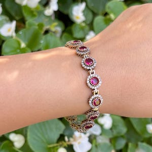 May include: A silver bracelet with a chain link design and round red gemstones surrounded by smaller clear gemstones.