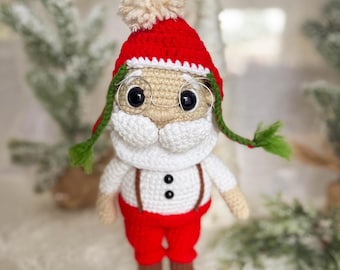 May include: A crocheted Santa Claus doll wearing a red hat with a white pom-pom, white beard, and round glasses. The doll is wearing red pants and white suspenders.
