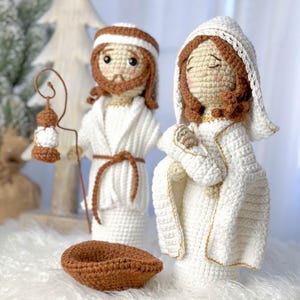 Puede incluir: Escena de la natividad tejida a crochet con un pesebre marrón, un José con túnica blanca sosteniendo un bastón de pastor, una María con túnica blanca sosteniendo un bebé Jesús y una linterna marrón.