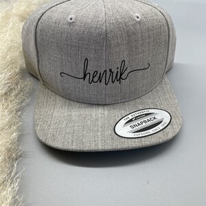 May include: Gray baseball cap with a black embroidered name "henrik" and a black and white "The Authentic Yupoong Snapback Since 1974" label.